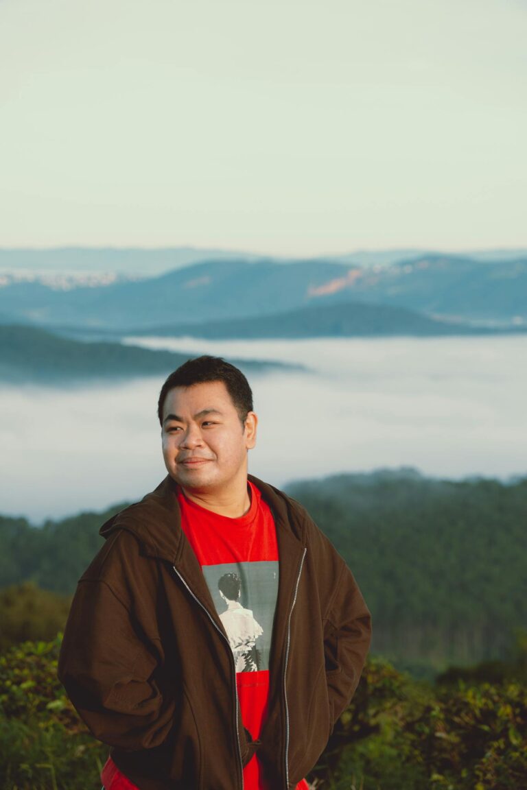 A man in a jacket enjoys a peaceful moment with a scenic view of Dalat mountains and clouds.
